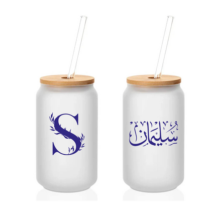 Two white tumblers with wooden lids and straws, one featuring a blue letter 'S' and the other with Arabic text.